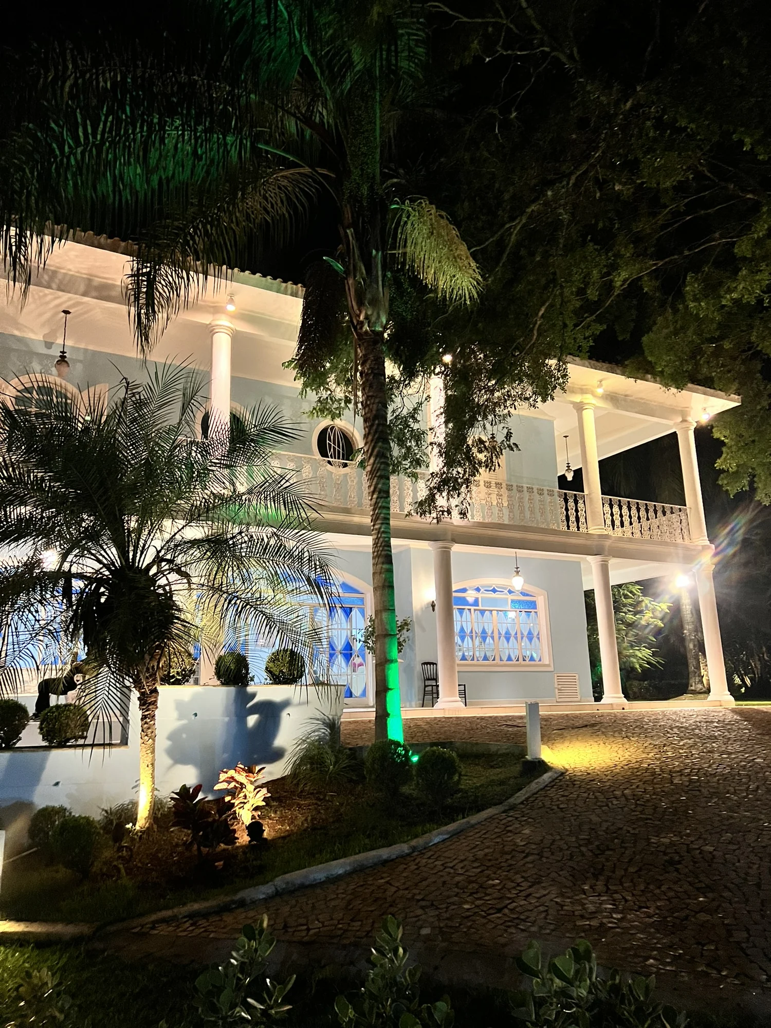 Fachada do casarão iluminada à noite, vista do jardim