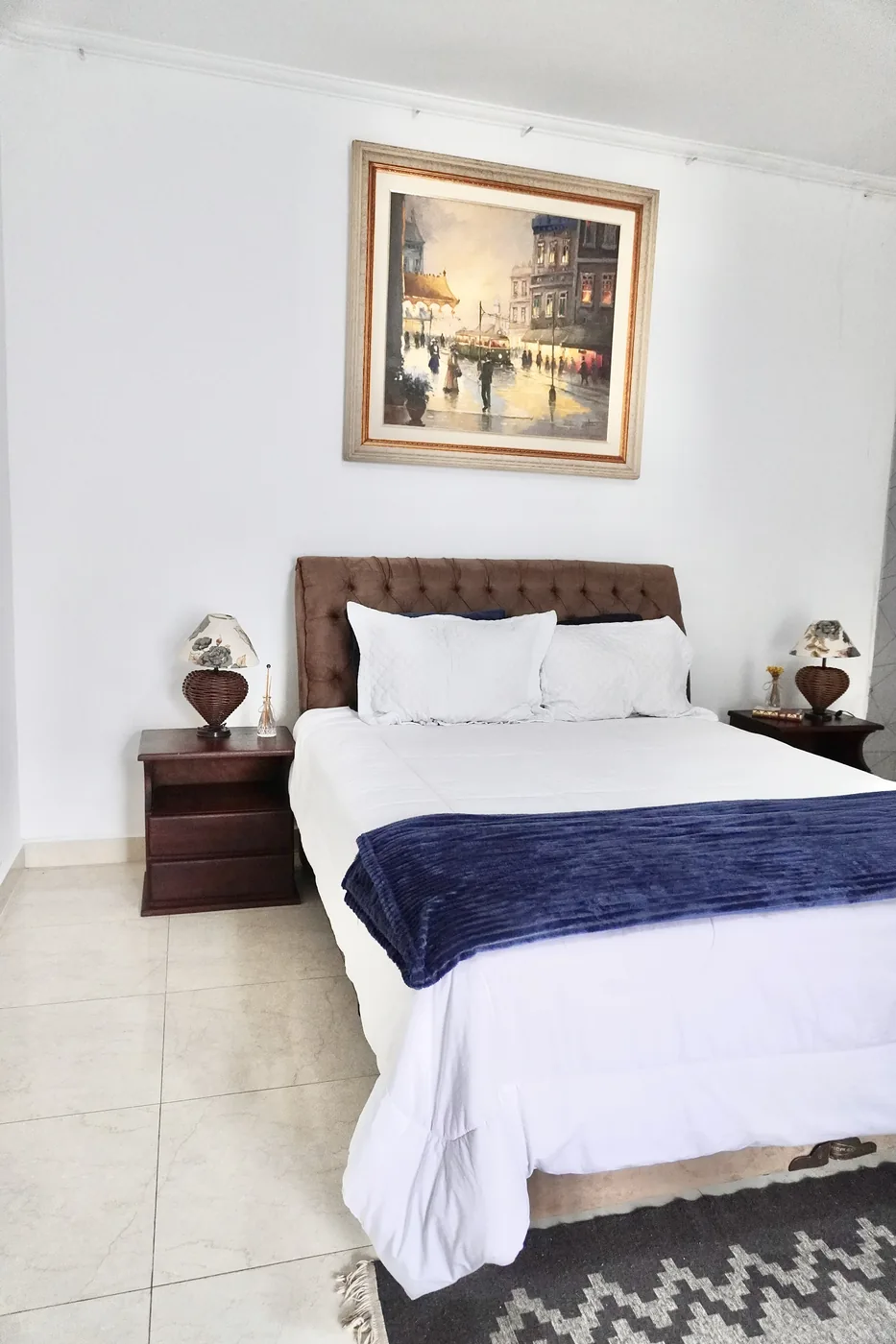 Cama de casal arrumada, com quadro sobre a cabeceira