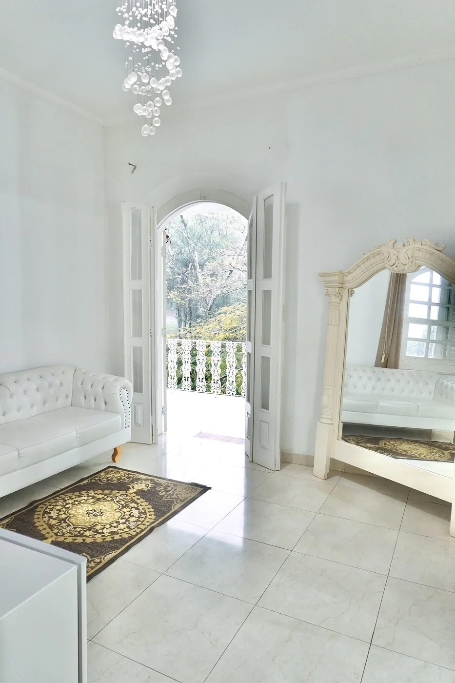Sala de estar com sofá branco e espelho, porta aberta para a varanda